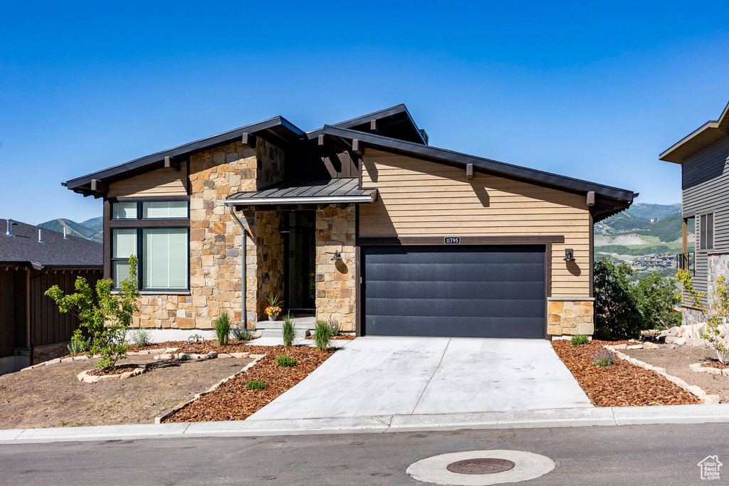 View of front of property featuring stone siding, driveway, a garage, a standing seam roof, and a metal roof