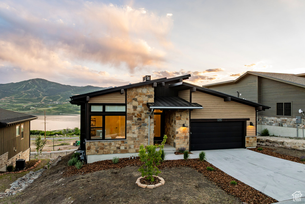 Modern home featuring stone siding, a garage, concrete driveway, a mountain view, and a metal roof