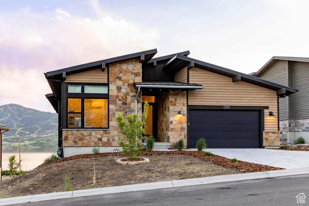 Modern home featuring stone siding, concrete driveway, a garage, and a standing seam roof