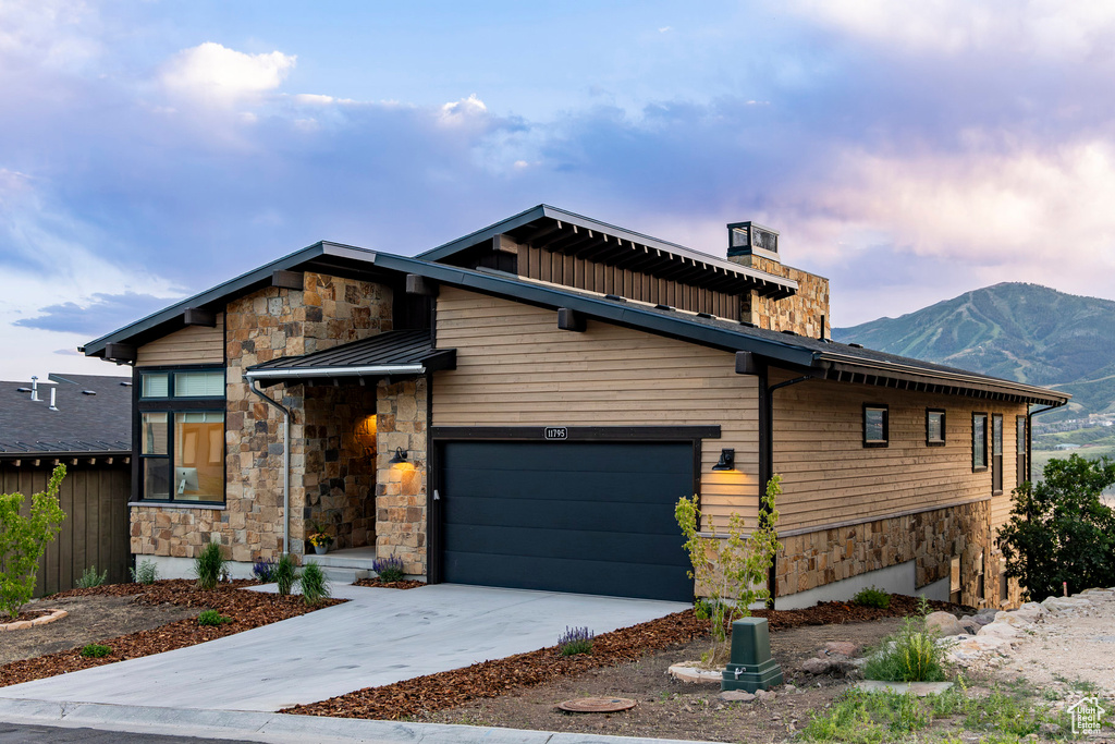 Contemporary house with stone siding, a standing seam roof, a mountain view, and driveway