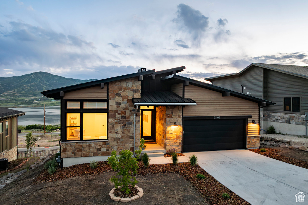 Modern home with stone siding, an attached garage, driveway, and a metal roof