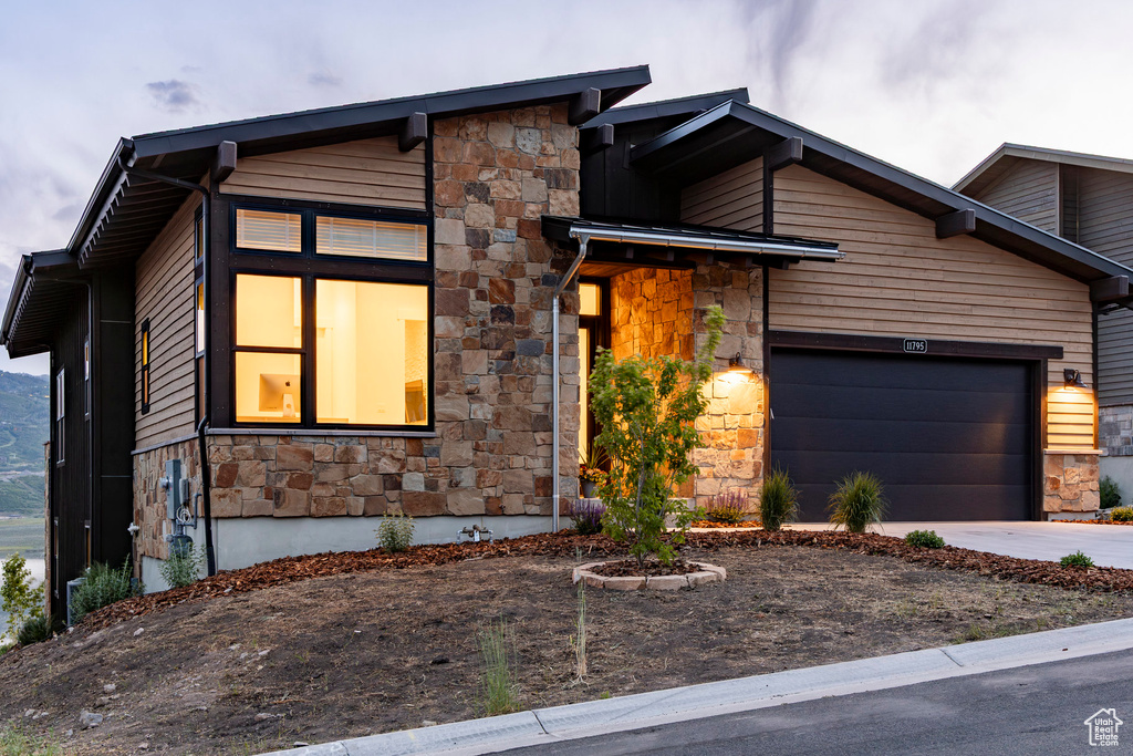Modern home featuring stone siding, driveway, and a garage