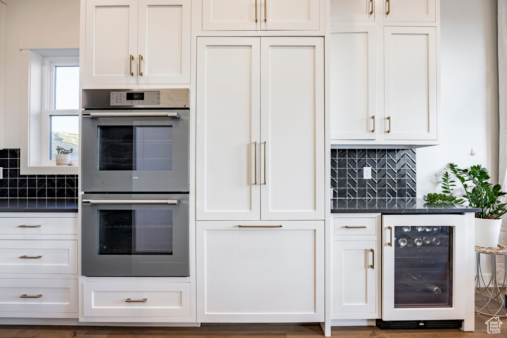 Kitchen featuring double oven, beverage cooler, dark countertops, and tasteful backsplash