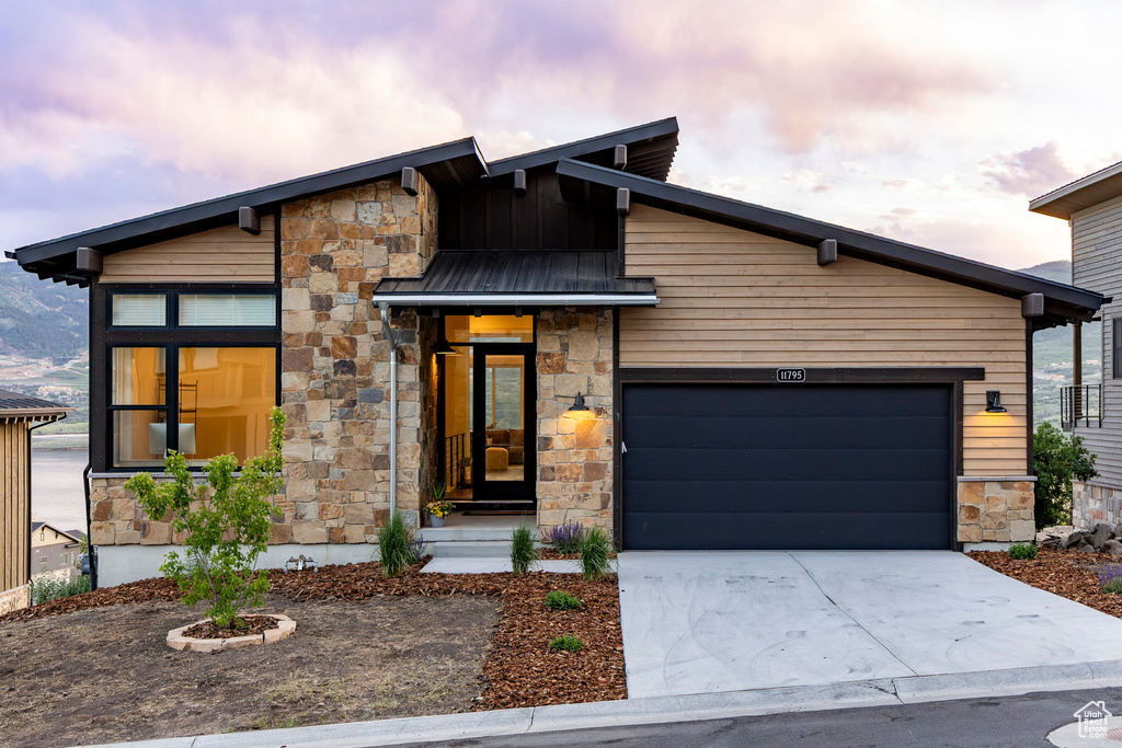 Contemporary house with stone siding, driveway, a garage, and a standing seam roof