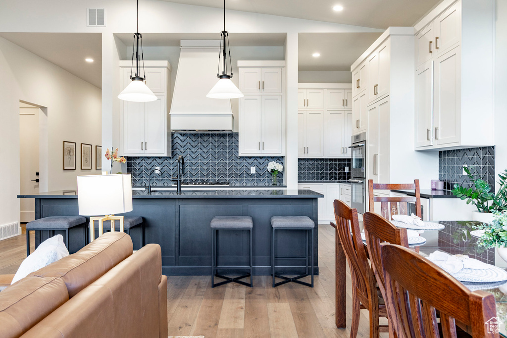 Kitchen featuring premium range hood, light wood-type flooring, white cabinetry, decorative backsplash, and recessed lighting
