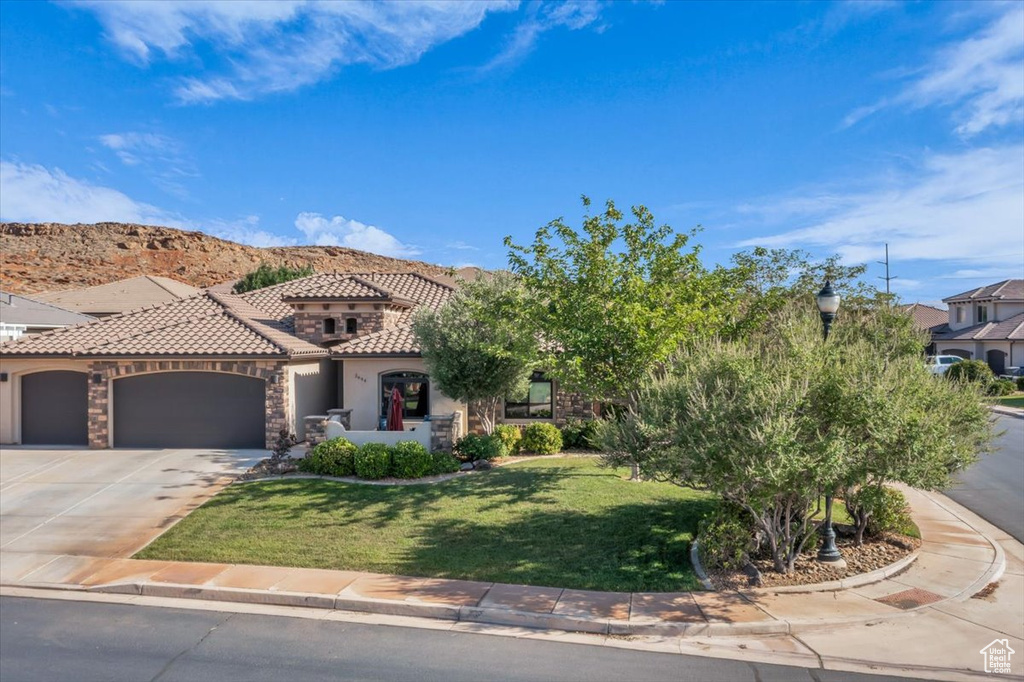 View of front of house featuring a tile roof, stucco siding, an attached garage, a front lawn, and driveway