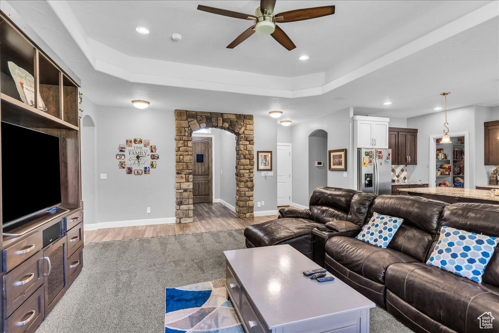 Living area featuring arched walkways, ceiling fan, light wood-style floors, a tray ceiling, and recessed lighting