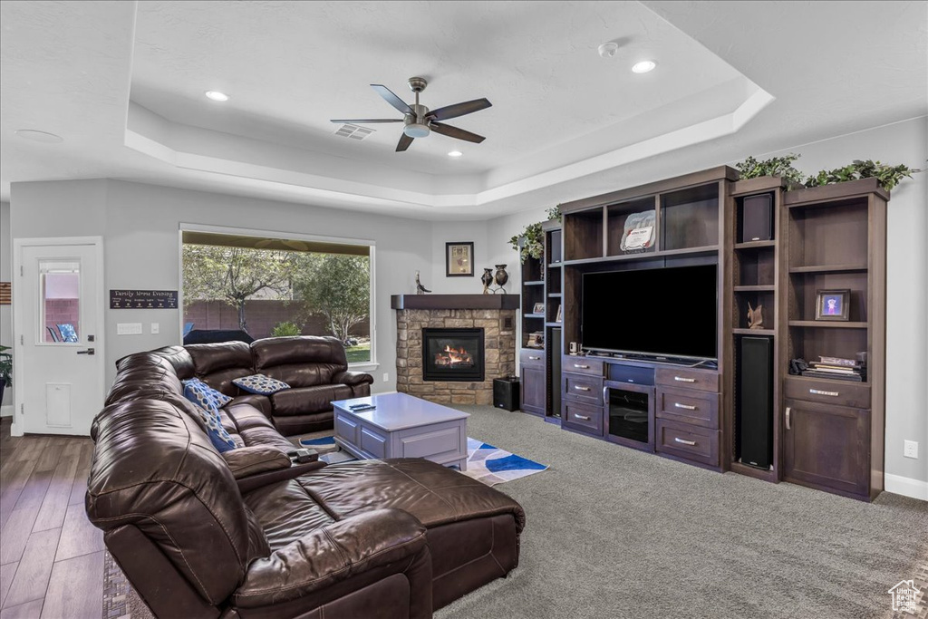 Living area with a tray ceiling, a ceiling fan, a stone fireplace, and recessed lighting