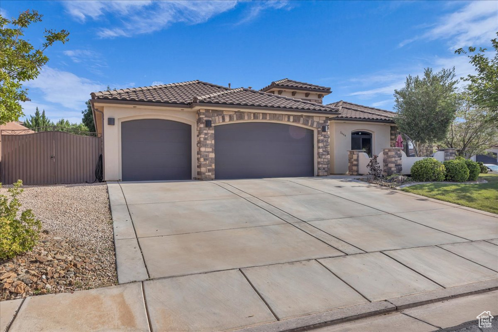Mediterranean / spanish-style house featuring a garage, a tile roof, stucco siding, a gate, and driveway