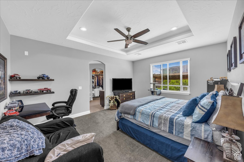 Carpeted bedroom featuring a raised ceiling, arched walkways, a ceiling fan, a spacious closet, and recessed lighting
