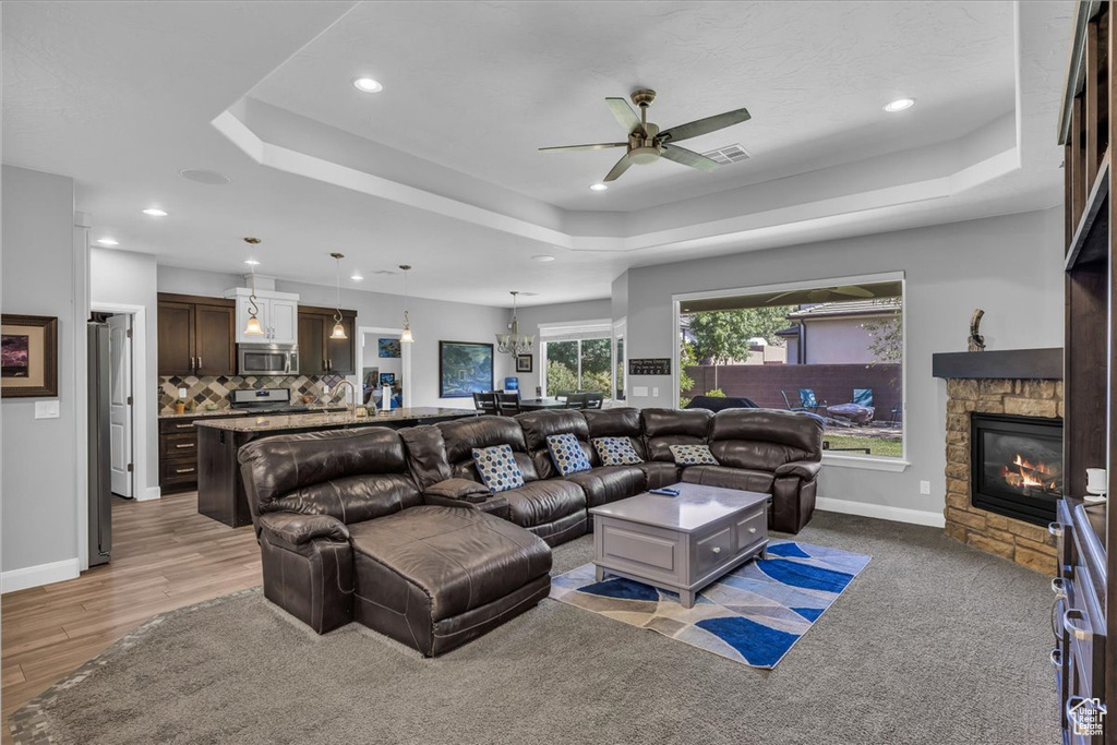 Living area featuring a tray ceiling, ceiling fan, a fireplace, recessed lighting, and light wood finished floors