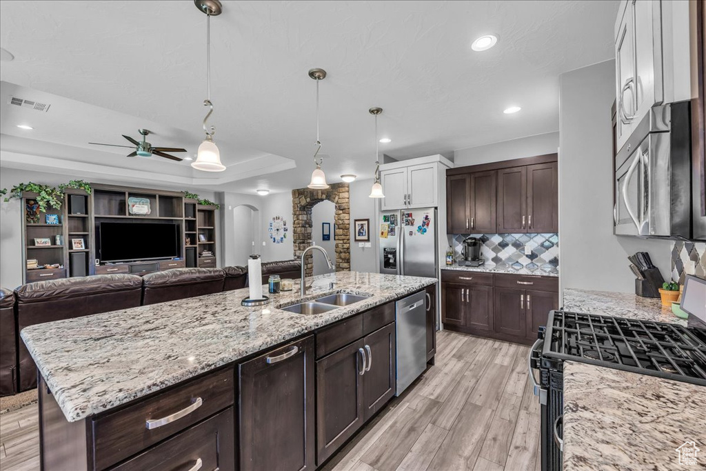 Kitchen featuring appliances with stainless steel finishes, open floor plan, ceiling fan, arched walkways, and tasteful backsplash