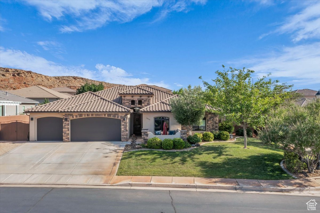 Mediterranean / spanish house with a garage, a front lawn, stucco siding, a tile roof, and concrete driveway