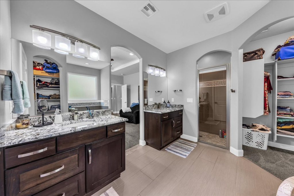 Full bathroom featuring a walk in closet, a shower stall, and two vanities