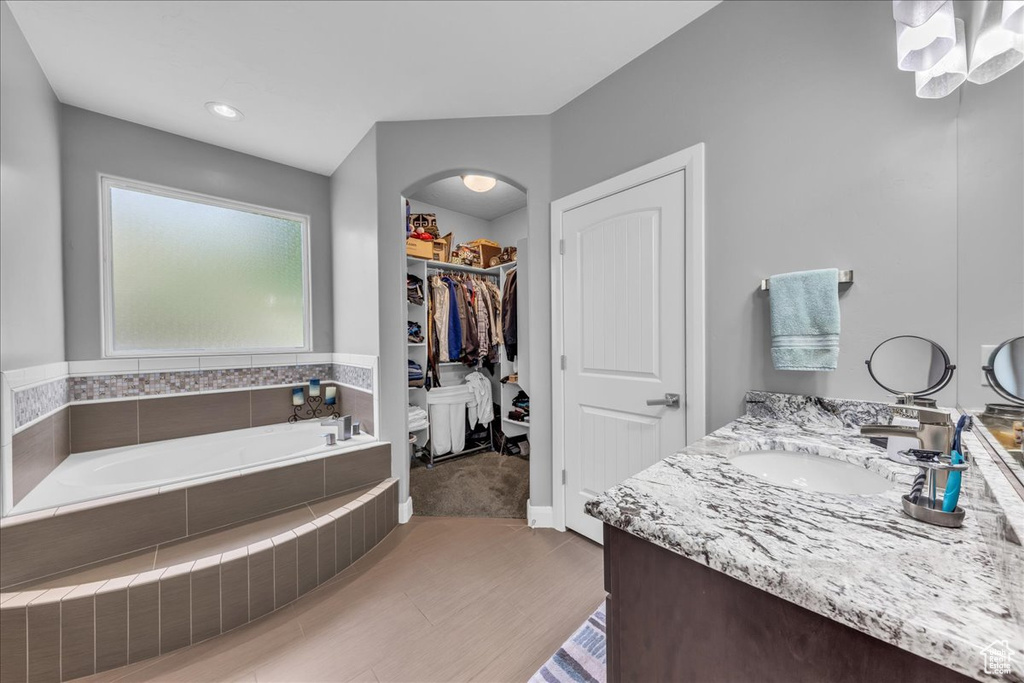 Full bath featuring a garden tub, double vanity, a spacious closet, and wood finished floors