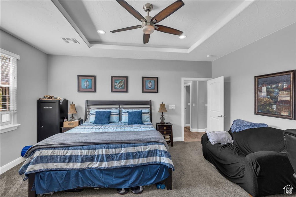 Carpeted bedroom with a raised ceiling, recessed lighting, and a ceiling fan
