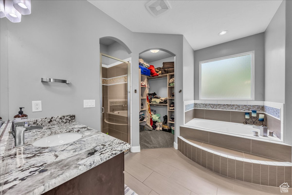 Full bath with a stall shower, a spacious closet, a garden tub, and vanity