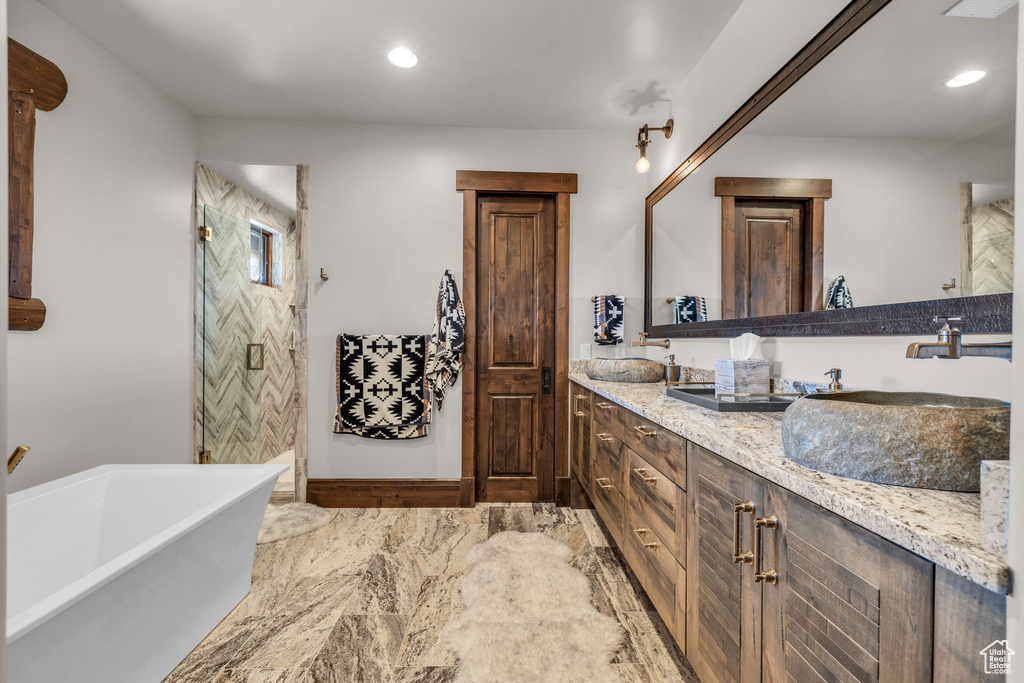 Full bath featuring double vanity, a soaking tub, marble finish floors, and recessed lighting