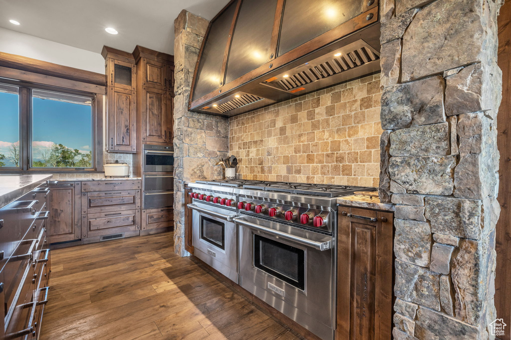 Kitchen with custom range hood, range with two ovens, tasteful backsplash, a warming drawer, and dark wood-type flooring