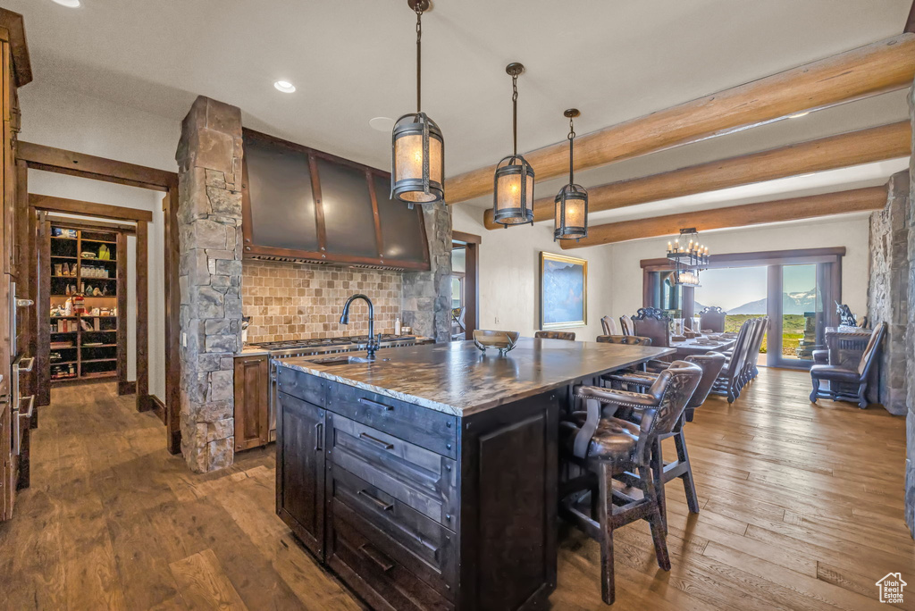 Kitchen featuring a kitchen breakfast bar, decorative backsplash, wood-type flooring, a center island with sink, and decorative light fixtures