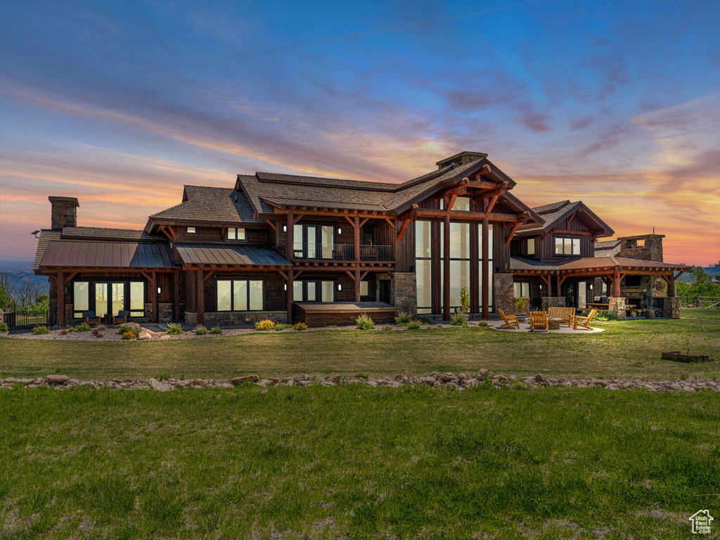 Rear view of property featuring a standing seam roof, stone siding, a chimney, a balcony, and a patio