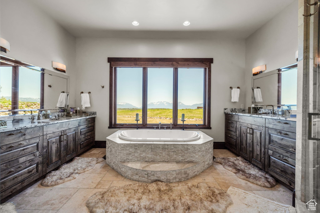 Full bath with stone tile floors, a bath, two vanities, and recessed lighting