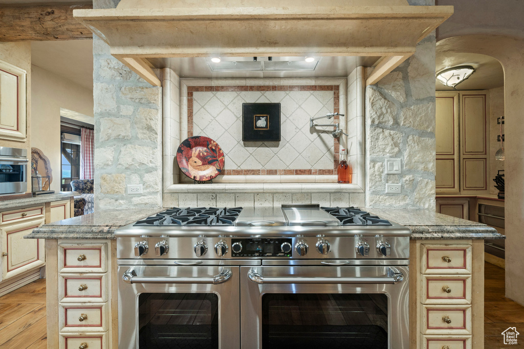Kitchen with stainless steel stove, cream cabinets, extractor fan, and light stone counters