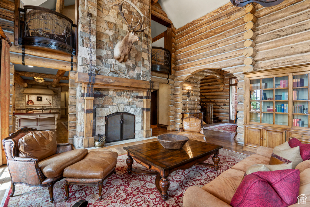 Living room with high vaulted ceiling, rustic walls, a stone fireplace, and wood finished floors