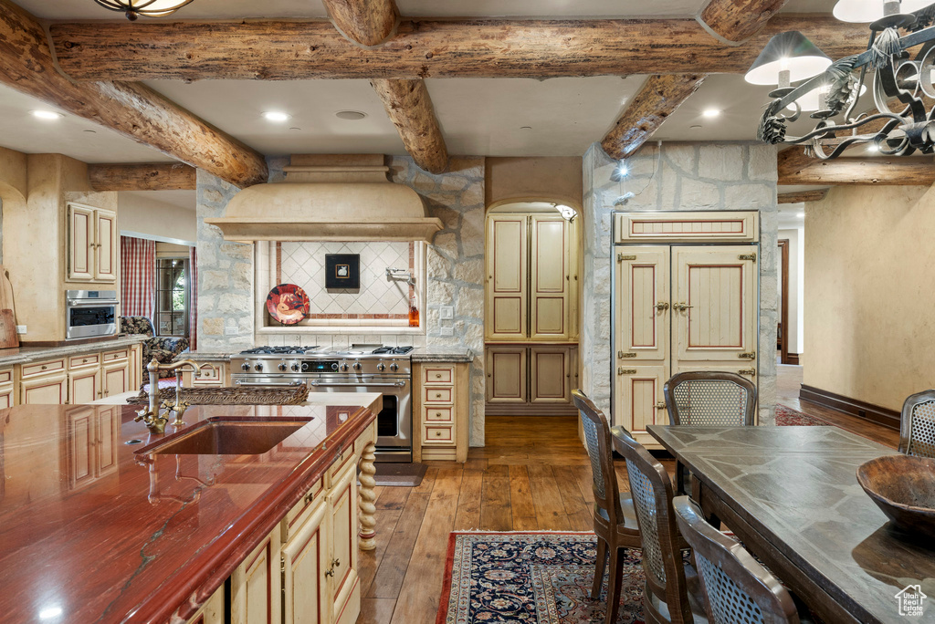 Kitchen featuring appliances with stainless steel finishes, wood-type flooring, beam ceiling, wooden counters, and cream cabinetry