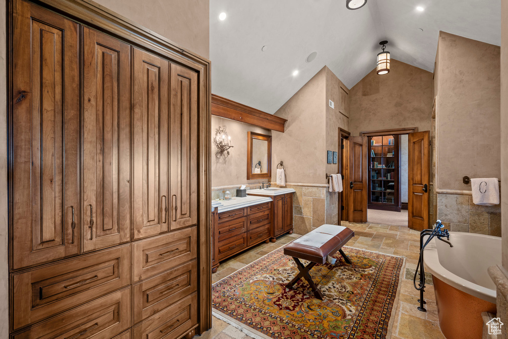 Bathroom featuring vanity, high vaulted ceiling, a soaking tub, and stone tile flooring
