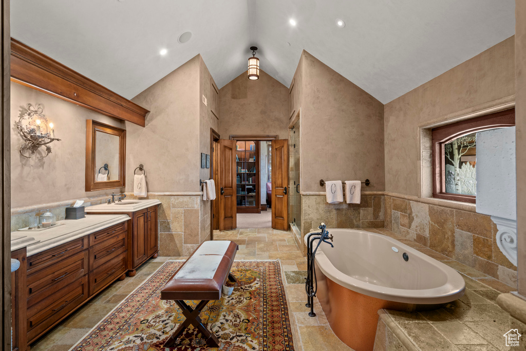 Bathroom featuring stone tile flooring, vanity, a tub, tile walls, and high vaulted ceiling