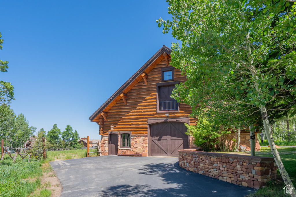 View of front of property with a barn, driveway, an attached garage, an outbuilding, and log siding