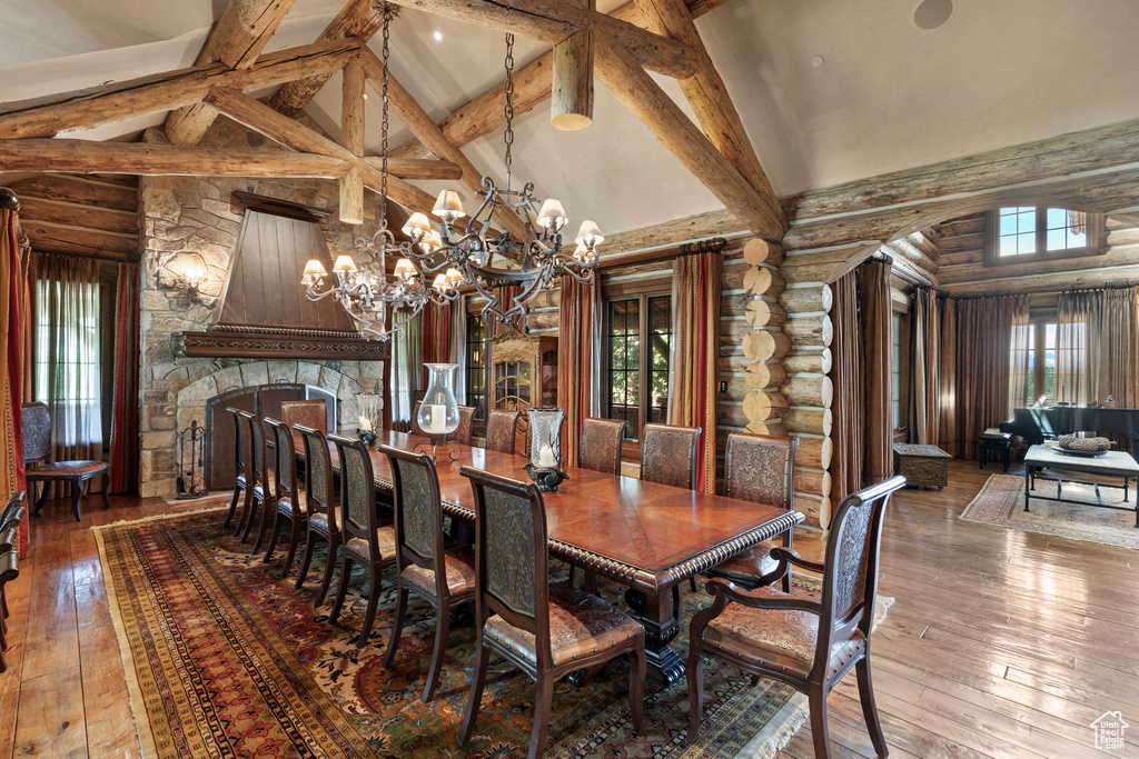Dining space with high vaulted ceiling, log walls, hardwood / wood-style floors, a chandelier, and beamed ceiling