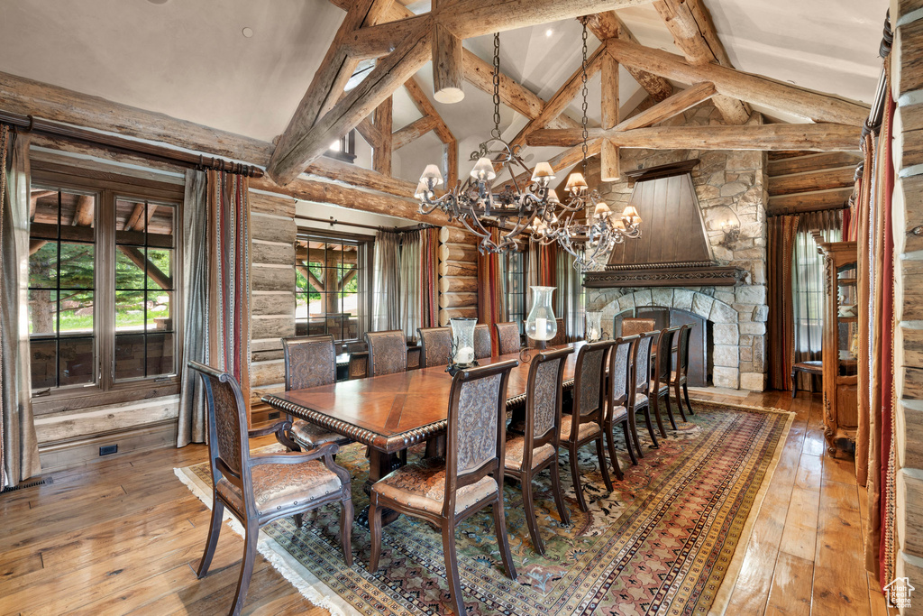 Dining space featuring hardwood / wood-style floors, a chandelier, high vaulted ceiling, beam ceiling, and a fireplace