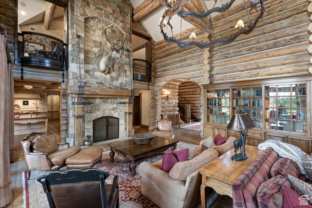 Living area with high vaulted ceiling, rustic walls, beam ceiling, wood finished floors, and a stone fireplace