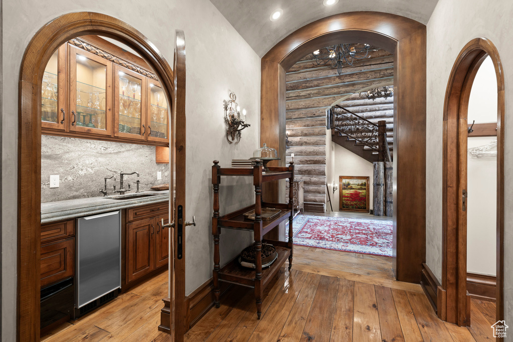 Wine cellar with light wood-style floors, rustic walls, arched walkways, and recessed lighting