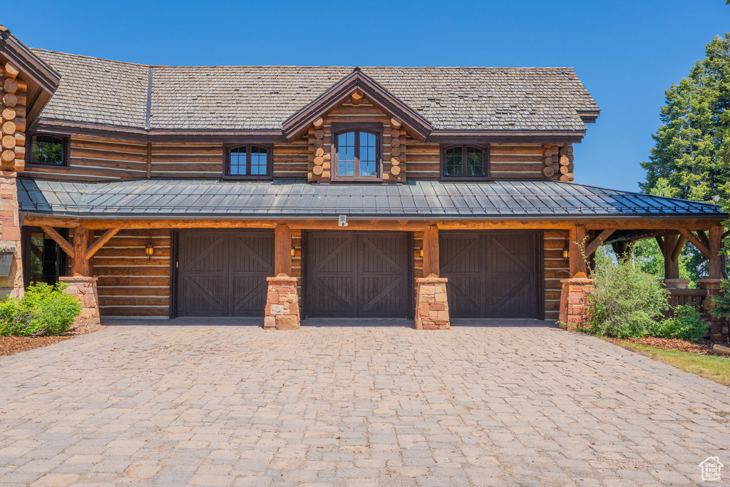 Log cabin featuring decorative driveway, a garage, log exterior, and a standing seam roof