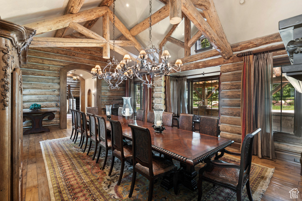 Dining space featuring rustic walls, arched walkways, high vaulted ceiling, healthy amount of natural light, and hardwood / wood-style flooring