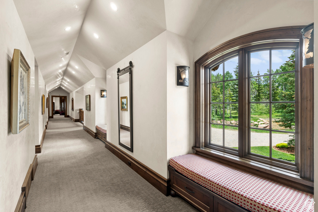 Corridor with vaulted ceiling, carpet floors, and a barn door