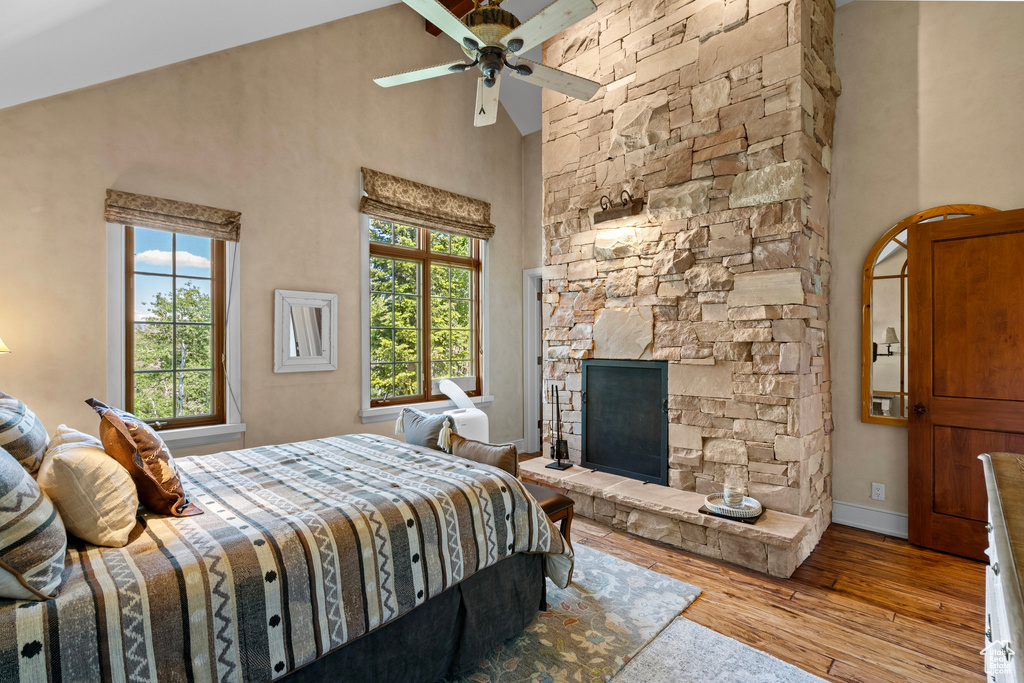 Bedroom with high vaulted ceiling, wood-type flooring, a stone fireplace, and a ceiling fan