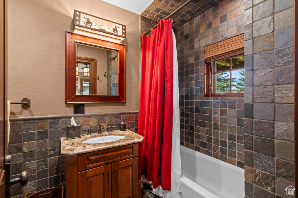 Full bathroom featuring tile walls, vanity, shower / bath combo with shower curtain, and a wainscoted wall