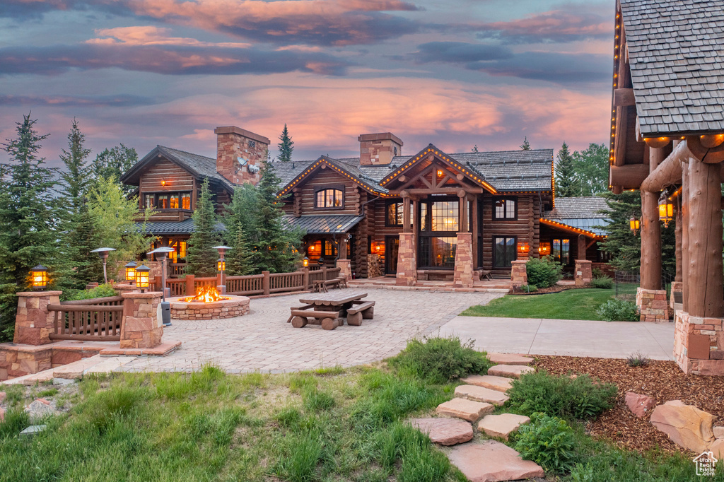 Back of property at dusk featuring an outdoor fire pit, a patio, a chimney, and log siding