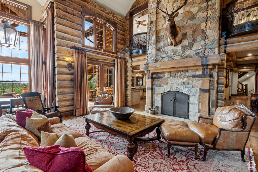 Living room featuring a towering ceiling, log walls, a fireplace, and wood finished floors