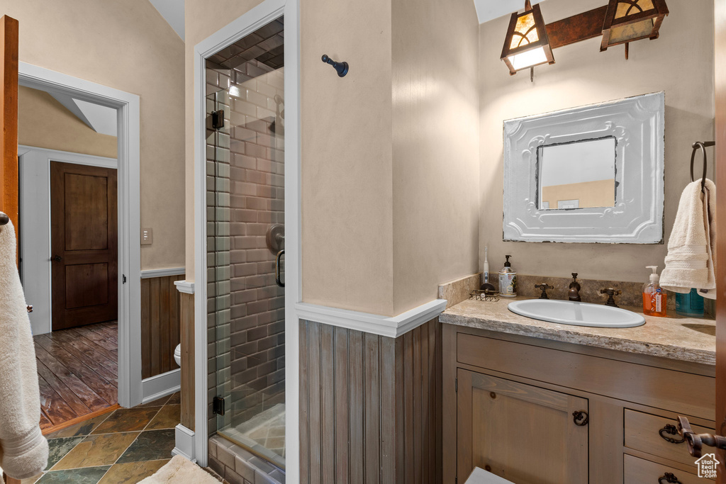 Bathroom with vanity, a stall shower, a wainscoted wall, and stone finish flooring