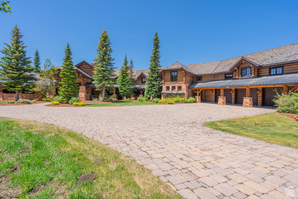 Log home with decorative driveway, log siding, and an attached garage