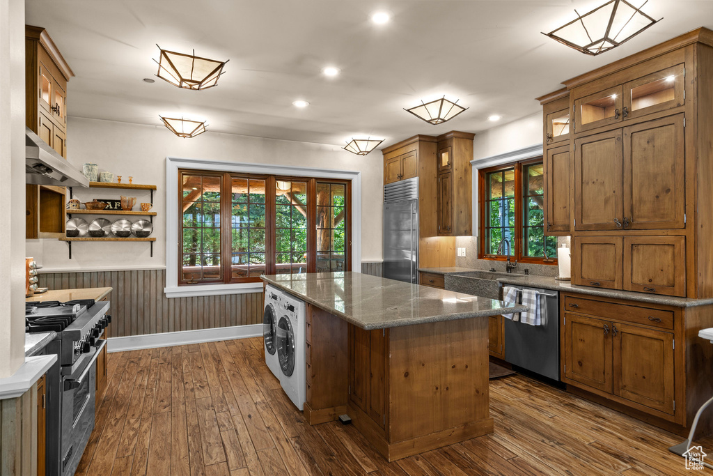 Kitchen featuring high end appliances, range hood, washer / dryer, a center island, and dark wood-style floors
