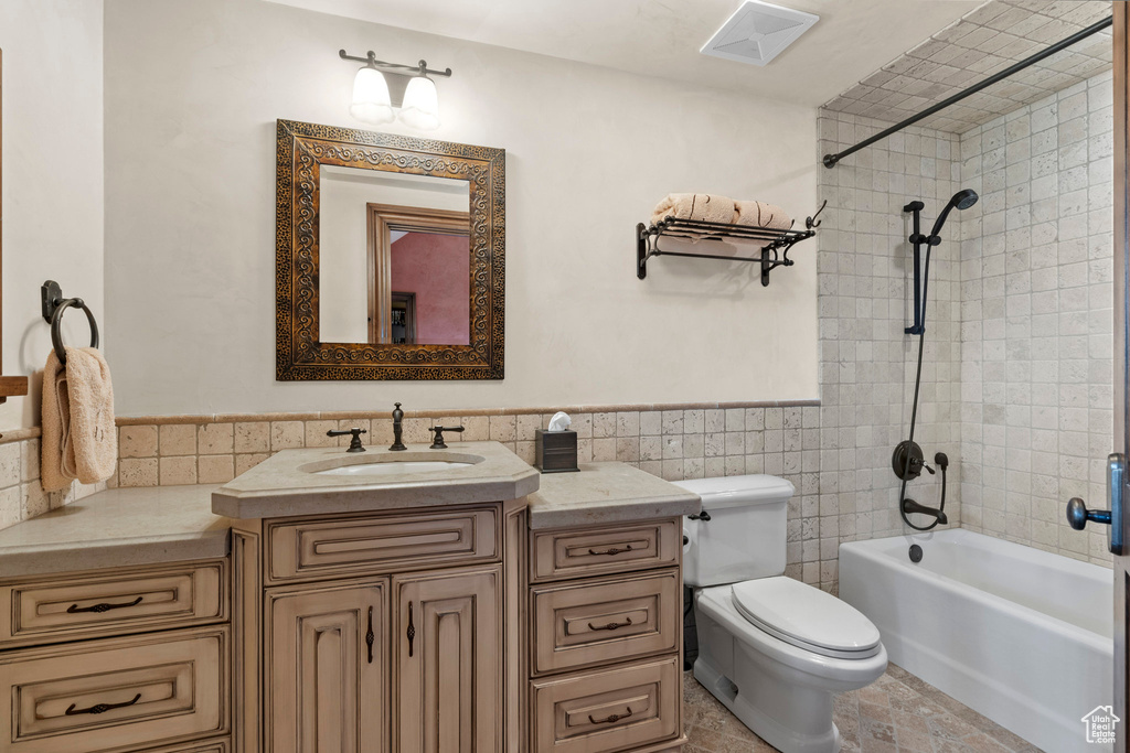 Full bathroom featuring tile walls, vanity,  shower combination, and wainscoting