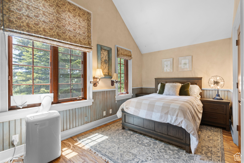 Bedroom with a wainscoted wall, wood finished floors, and high vaulted ceiling