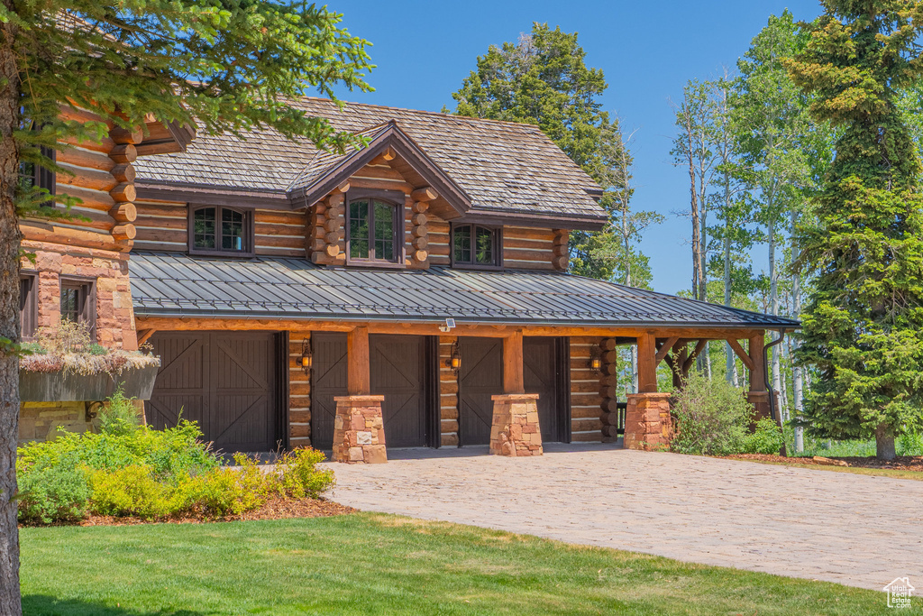 Log-style house with log exterior, an attached garage, driveway, a standing seam roof, and a front lawn