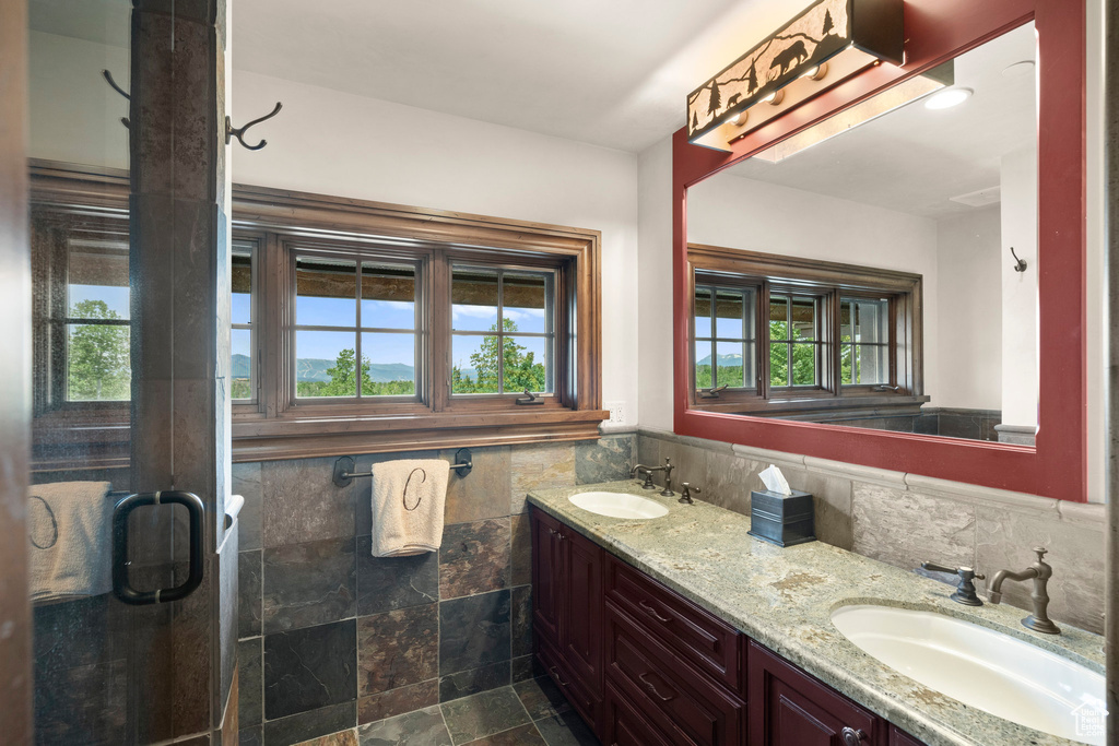 Bathroom with double vanity, healthy amount of natural light, tile walls, wainscoting, and a stall shower
